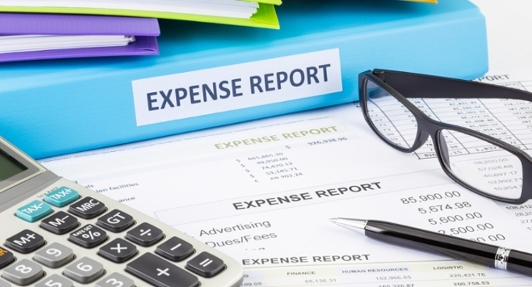 One binder sits atop a table of papers. It is labeled as "expense reports."